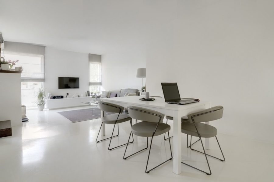 Heller Wohnraum mit hellem Epoxidboden von Epoxyka. Es stehen ein Fernseher und ein Tisch mehreren Stühlen.